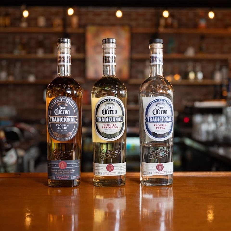 Three Jose Cuervo Tradicional tequila bottles displayed on a polished bar counter in a warmly lit restaurant.